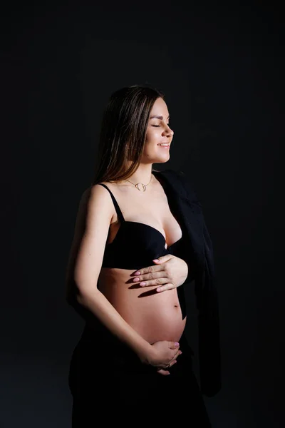 Elegant pregnant woman. Beautiful pregnant girl with long hair in black suit on gray background, concept of happy pregnancy and family.