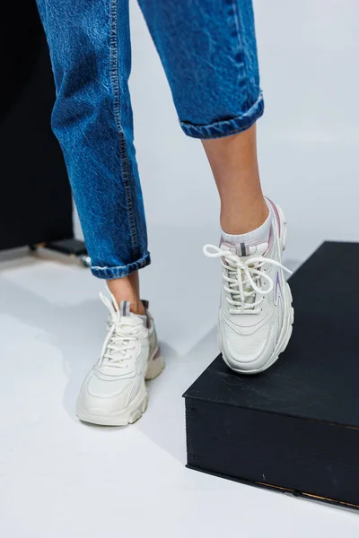 Casual women's fashion. Sports shoes for women. Slender female legs in jeans and white stylish casual sneakers. Women's comfortable summer shoes.