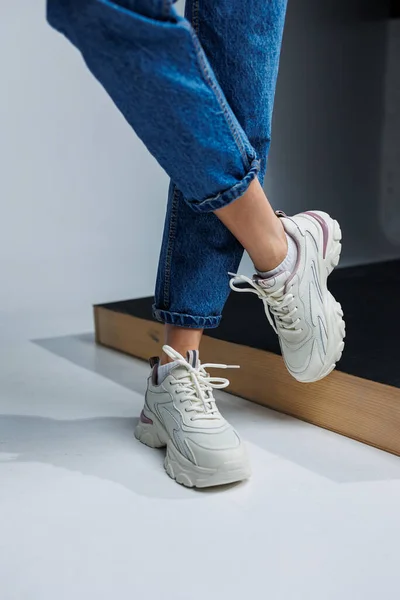 Casual women\'s fashion. Sports shoes for women. Slender female legs in jeans and white stylish casual sneakers. Women\'s comfortable summer shoes.