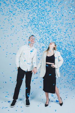 Mavi konfetide sarılan genç ve mutlu bir çift. Birbirine aşık bir çift neşelenir ve eğlenir. Cinsiyet fotoğraf oturumu