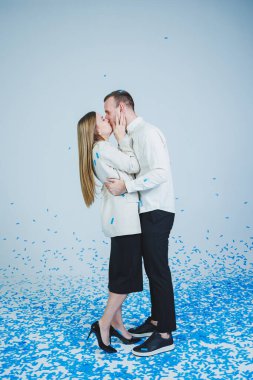 Mavi konfetide sarılan genç ve mutlu bir çift. Birbirine aşık bir çift neşelenir ve eğlenir. Cinsiyet fotoğraf oturumu