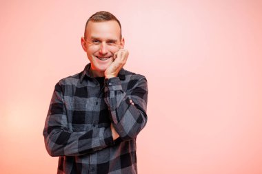 Pembe arka planda kareli gömlekli, gülümseyen genç bir adam. Metin için yer