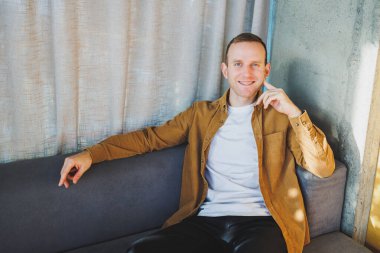 Geniş, modern bir ofiste uzaktan çalışan gülümseyen genç serbest çalışan bir erkek. Rahat giyimli bir yönetici ofiste rahat çalışır..