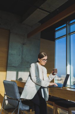 Ofis işleri, ofiste çalışan çekici genç bayan yöneticiler modern dizüstü bilgisayarla parlak çalışma alanları, lezzetli kahve içen genç kadınlar.