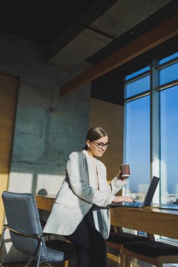 Ofis işleri, ofiste çalışan çekici genç bayan yöneticiler modern dizüstü bilgisayarla parlak çalışma alanları, lezzetli kahve içen genç kadınlar.