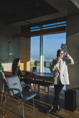 Ofis işleri, ofiste çalışan çekici genç bayan yöneticiler, modern dizüstü bilgisayarla parlak çalışma alanları, dizüstü bilgisayarla video görüşmesi yapan genç kızlar.