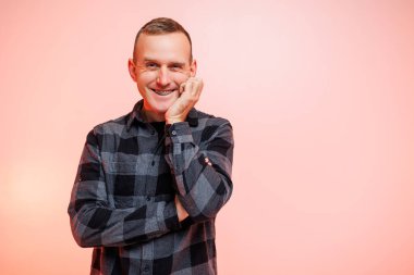 Pembe arka planda kareli gömlekli, gülümseyen genç bir adam. Metin için yer