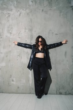 Gri arka planda poz veren zarif deri takım elbiseli, pantolon, ceket, şık güneş gözlüğü takan zarif genç kadın modeller..