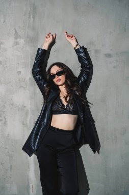 Gri arka planda poz veren zarif deri takım elbiseli, pantolon, ceket, şık güneş gözlüğü takan zarif genç kadın modeller..