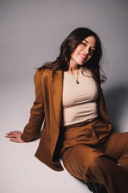 Gri arka planda poz veren şık kahverengi takım elbiseli güzel, zarif genç bayan modeller. Takım elbiseli zarif bir bayan.