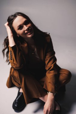 Gri arka planda poz veren şık kahverengi takım elbiseli güzel, zarif genç bayan modeller. Takım elbiseli zarif bir bayan.