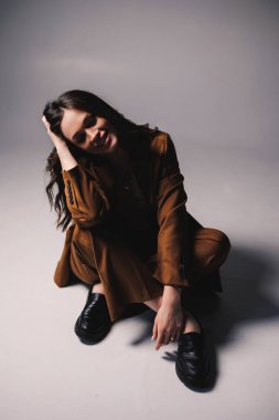 Gri arka planda poz veren şık kahverengi takım elbiseli güzel, zarif genç bayan modeller. Takım elbiseli zarif bir bayan.