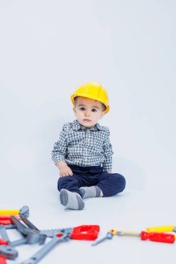 Kareli tişörtlü küçük bir çocuk müteahhit suretinde. İnşaat kaskı ve plastik aletleri olan bir çocuk.