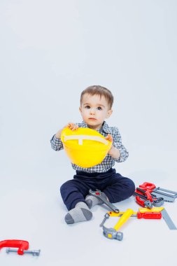 Kareli tişörtlü küçük bir çocuk müteahhit suretinde. İnşaat kaskı ve plastik aletleri olan bir çocuk.