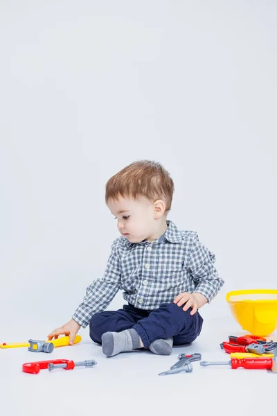 stock image A little boy in a shirt with a helmet and a toy tool. White background. Toy construction tool for children