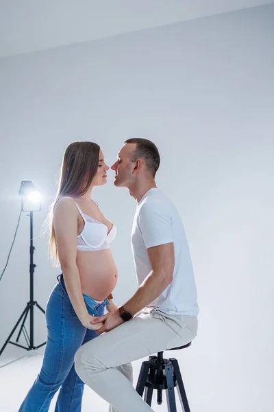 幸福的年轻夫妇期待着一个白色的T恤衫和牛仔裤白色背景的孩子 怀孕和分娩的快乐 一对幸福的夫妻正在期待着一个孩子 — 图库照片