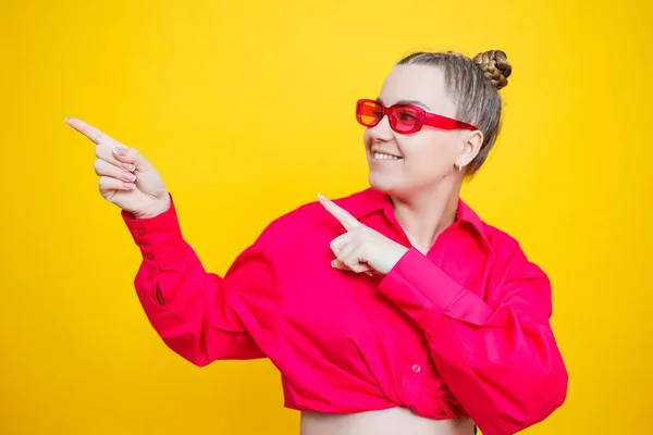 Happy pregnancy. Cheerful pretty pregnant woman in a pink shirt and pink glasses on a yellow background. Young bright pregnant woman.