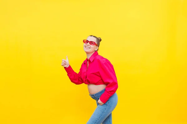 stock image A smiling pregnant woman in a pink cotton shirt and jeans gently holds her pregnant belly. Posing for the camera. Concept of easy and happy pregnancy.