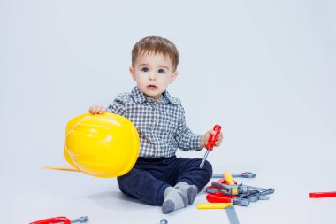 Kasklı ve oyuncak aletli tişörtlü küçük bir çocuk. Beyaz arka plan. Çocuklar için oyuncak yapım aracı
