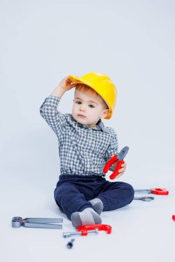 Beyaz arka planda, bir müteahhit kılığında tişörtlü şirin bir çocuk. Çocukluk, öğrenme, çalışma, oyunlar, kariyer, taklit. Küçük babanın yardımcısı..