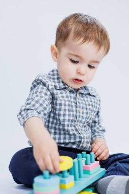 Gömlekli küçük bir çocuk beyaz arka planda renkli ahşap bir oyuncak yapıyor. Çocuk gelişimi konsepti, çocuklar için oyunlar, oyuncaklar. Boşluğu kopyala