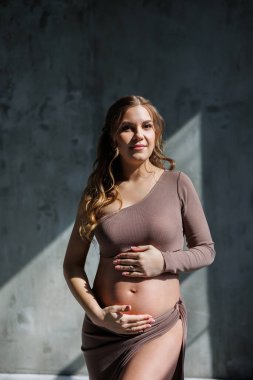 Kahverengi narin takım elbiseli mutlu, hamile bir kadın karnını okşayıp poz veriyor. Hamile hamile bir kadın. Mutlu hamilelikler