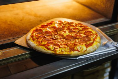 Fırından taze pizzayı metal bir spatulayla çıkarıyorum..