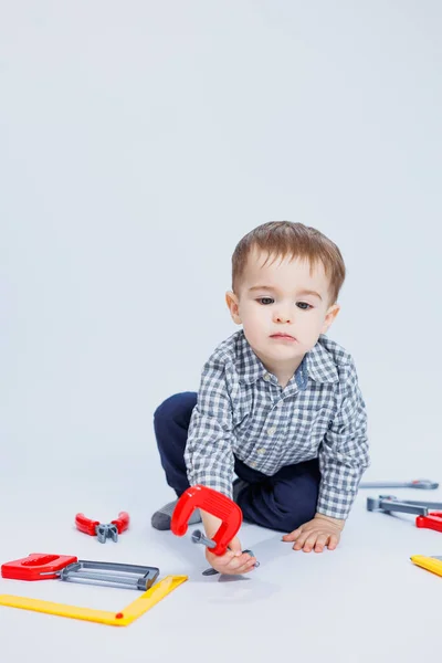 A cute boy in a shirt in the image of a builder, on a white background. Childhood, learning, work, games, career, imitation. Little daddy\'s helper.