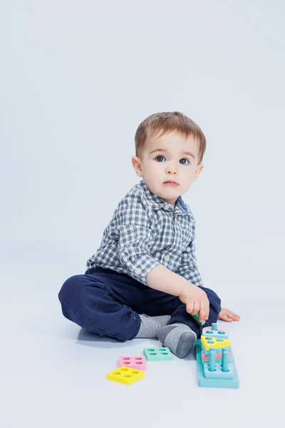 小さな男の子が白い背景に座って 木製の教育用おもちゃで遊んでいます 子供のための生態木製玩具 — ストック写真