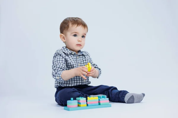 stock image A little boy in a shirt is building a colorful wooden toy on a white background. The concept of children's development, games for children, toys. Copy space