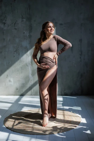 A happy young pregnant woman in a brown delicate suit is posing and stroking her belly. Pregnant pregnant woman. Happy pregnancy