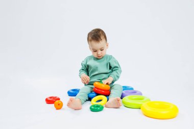 Beyaz arka planda plastik eğitim oyuncaklarıyla oturan neşeli küçük çocuk. Gelişim için çocuk ve oyuncaklar. Çocukların motor becerilerinin gelişimi.