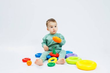 Beyaz arka planda plastik eğitim oyuncaklarıyla oturan neşeli küçük çocuk. Gelişim için çocuk ve oyuncaklar. Çocukların motor becerilerinin gelişimi.