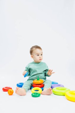 Beyaz arka planda plastik eğitim oyuncaklarıyla oturan neşeli küçük çocuk. Gelişim için çocuk ve oyuncaklar. Çocukların motor becerilerinin gelişimi.