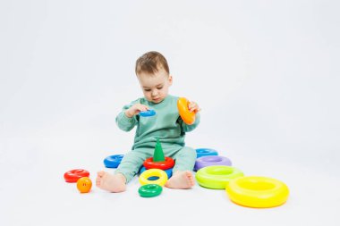 Beyaz arka planda plastik eğitim oyuncaklarıyla oturan neşeli küçük çocuk. Gelişim için çocuk ve oyuncaklar. Çocukların motor becerilerinin gelişimi.