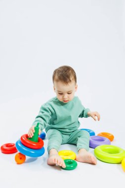 Beyaz arka planda plastik eğitim oyuncaklarıyla oturan neşeli küçük çocuk. Gelişim için çocuk ve oyuncaklar. Çocukların motor becerilerinin gelişimi.