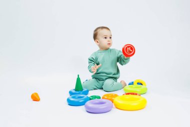 Beyaz arka planda plastik eğitim oyuncaklarıyla oturan neşeli küçük çocuk. Gelişim için çocuk ve oyuncaklar. Çocukların motor becerilerinin gelişimi.