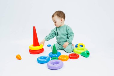 Beyaz arka planda plastik eğitim oyuncaklarıyla oturan neşeli küçük çocuk. Gelişim için çocuk ve oyuncaklar. Çocukların motor becerilerinin gelişimi.