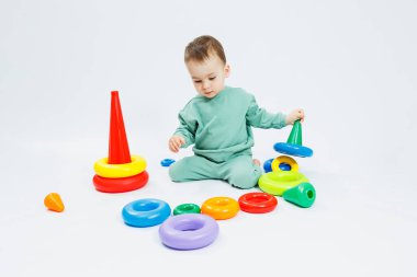 Beyaz arka planda plastik eğitim oyuncaklarıyla oturan neşeli küçük çocuk. Gelişim için çocuk ve oyuncaklar. Çocukların motor becerilerinin gelişimi.