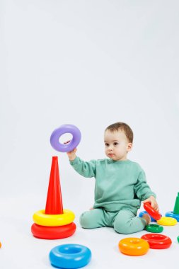 Beyaz arka planda izole edilmiş plastik piramitle mantık oyunu oynayan küçük çocuk. Mutlu bir çocuk eğitici bir oyuncakla oynar. Bebek bir yıl dört aylık.