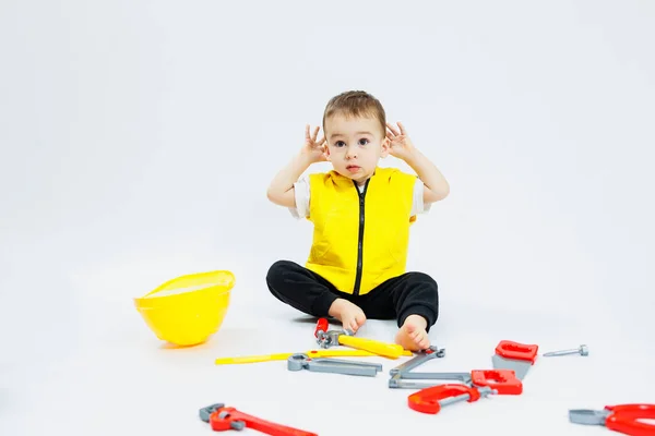 Stock image A little boy 2 years old in a builder's suit on a white background. A child in a plastic helmet and plastic tools. Plastic children's toys.