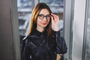 Gözlüklü gülümseyen bir kadının portresi. Pencerenin yanındaki genç iş kadını.