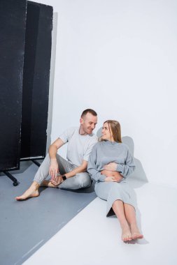 Genç ve mutlu bir çift hamilelikten ve beyaz bir arka planda sarılmaktan mutlu. Mutlu bir karı koca hamile ve bir çocuk bekliyorlar..