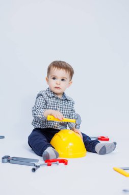 Küçük bir çocuk beyaz bir arka planda bir oyuncak set inşaatçı aletleriyle oynuyor. Çocuk plastik oyuncakları..