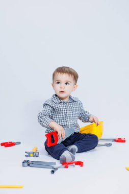 Küçük bir çocuk beyaz bir arka planda bir oyuncak set inşaatçı aletleriyle oynuyor. Çocuk plastik oyuncakları..