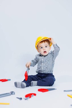 Küçük bir çocuk beyaz bir arka planda bir oyuncak set inşaatçı aletleriyle oynuyor. Çocuk plastik oyuncakları..