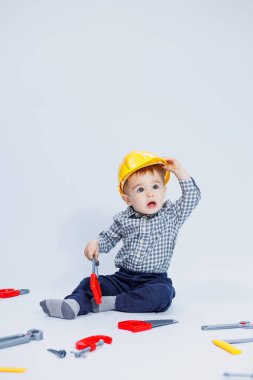 Küçük bir çocuk beyaz bir arka planda bir oyuncak set inşaatçı aletleriyle oynuyor. Çocuk plastik oyuncakları..