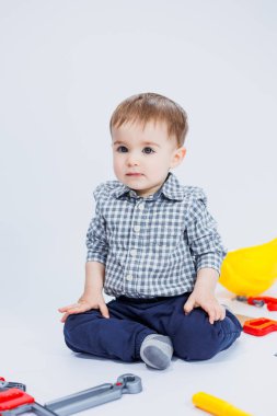 Küçük bir çocuk beyaz bir arka planda bir oyuncak set inşaatçı aletleriyle oynuyor. Çocuk plastik oyuncakları..