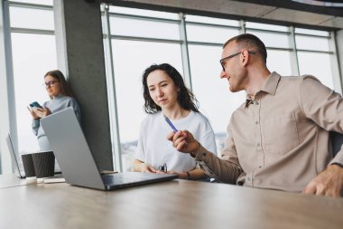 Büyük pencereli bir ofiste çalışmak, meslektaşlar taşınabilir bir dizüstü bilgisayar kullanarak yeni bir proje üzerinde çalışıyorlar. Çalışanlarla modern ofis.