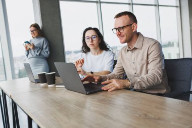 Büyük pencereli bir ofiste çalışmak, meslektaşlar taşınabilir bir dizüstü bilgisayar kullanarak yeni bir proje üzerinde çalışıyorlar. Çalışanlarla modern ofis.